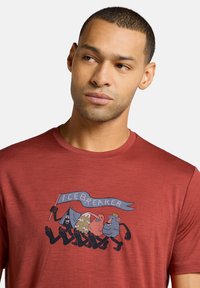 Rotes T-Shirt mit kurzen Ärmeln aus weichem Stoff, das eine spielerische Grafik von bunten, cartoonhaften Figuren und einem blauen Banner mit der Aufschrift "ICEBREAKER" zeigt.