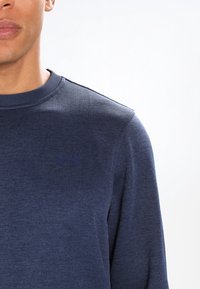 Camicia a maniche lunghe blu navy realizzata in tessuto texturizzato; presenta una scollatura girocollo e un piccolo logo sul petto.