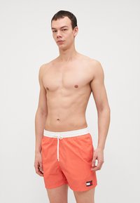 Şorturi de baie pentru bărbați, de culoare portocalie, dintr-un material ușor, cu un tiv elastic alb și șnur de reglare, având un patch cu logo pe lateral.