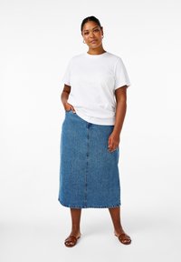 Camiseta blanca de manga corta, falda midi de mezclilla azul y sandalias marrones. La falda tiene un corte recto y bolsillos laterales, con una textura suave.