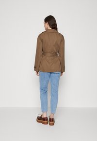 Bruine riem blazer met een klassieke kraag, achterste split en knoopmanchetten, gecombineerd met lichtblauwe denim jeans en stevige bruine platform schoenen.