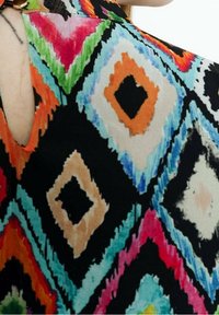 Färgglad top med ett diamantmönster i svart, orange, rosa, teal och beige nyanser, samt en cutout-detalj i ryggen. Tyget verkar lätt.