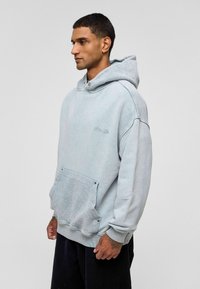 Lichtblauwe oversized hoodie van zachte stof, met een trekkoord capuchon, voorzak en ribgebreide manchetten. Subtiele logo-detail op de borst.