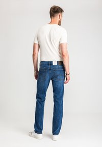 Ciemnoniebieskie jeansy z denimu o prostym kroju nogawek, z klasycznym wzorem pięciu kieszeni i detalami przeszyć, noszone z białym t-shirtem.