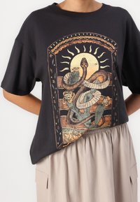 Sort bomulds t-shirt med et farverigt grafik af slanger og blomster, rund halsudskæring og korte ærmer med en afslappet pasform.