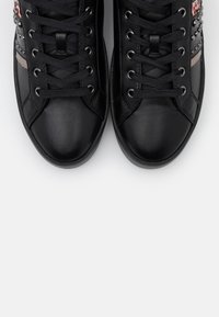 Schwarze Leder-Sneaker mit flachen schwarzen Schnürsenkeln, ausgestattet mit einer strukturierten Fläche und Nietenakzenten an den Seiten. Abgerundete Zehenpartie und Gummisohle.