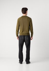 Olijfgroene gebreide trui met lange mouwen en geribbelde manchetten, gecombineerd met zwarte recht-toe-rechtdoor jeans en zwarte schoenen. Minimalistisch ontwerp.