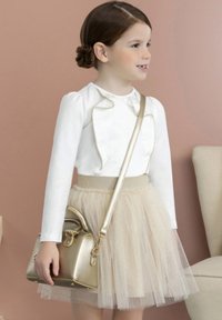 Maglia bianca a maniche lunghe con dettagli a volant, gonna in tulle beige e una piccola borsa metallizzata oro. Sfondo neutro, bambino in piedi.