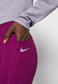 Nike sportovní legíny v živé fialové barvě, s boční kapsou a šedým logem. Vrchní díl je dlouhý rukáv, světle šedý, melírovaný materiál.