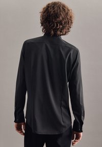 Camicia nera a maniche lunghe con una texture liscia, polsini con bottoni e vestibilità sartoriale, caratterizzata da un orlo curvo e design minimalista.