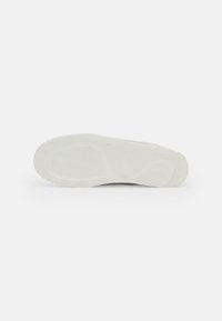 Semelle de chaussure de sport en caoutchouc blanc, présentant un motif de semelle en chevrons et des designs courbés pour une meilleure adhérence, avec une finition lisse.