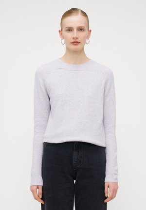 Un pull violet clair avec un col ras du cou, des manches raglan longues, des poignets côtelés et une texture douce, associé à un jean noir taille haute.