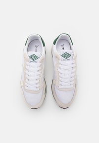Baskets Lacoste avec tige en mesh blanche, accents en daim beige, logo vert et semelle en caoutchouc noire, dotées de lacets blancs et d'un col rembourré.