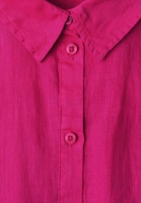 Chemise en lin rose vif avec col pointu et trois boutons assortis sur la patte de boutonnage avant.