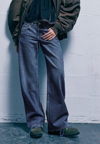 Vida jeans i mörkblå denim med subtilt färgspel. Matchas med gröna snörskor med texturerad sula.