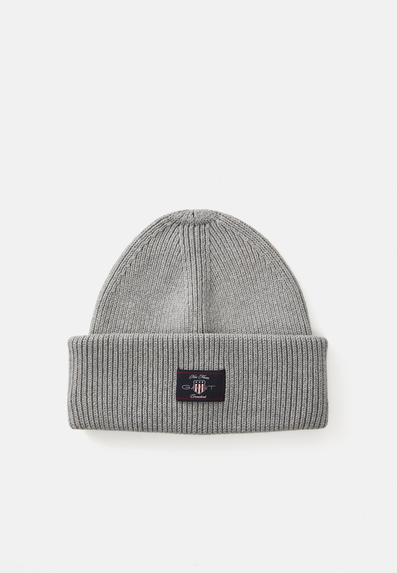 Bonnet en tricot côtelé gris avec un revers et un patch logo noir aux accents rouges et blancs. Texture douce et forme ajustée.