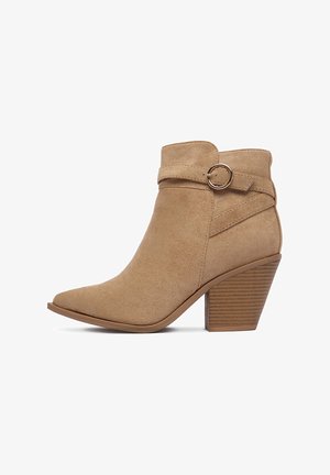 Béžové semišové členkové topánky so sukovitým špicom a opleteným pásikom s kruhovým akcentom. Masívny, ryhovaný podpätok pre stabilitu.