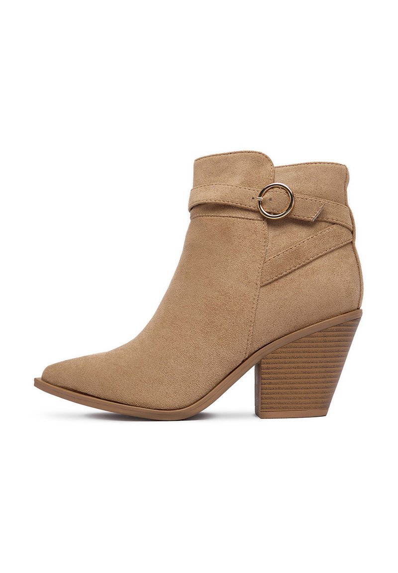 Beżowy zamszowy botek za kostkę z szpiczastym noskiem i owiniętym paskiem z okrągłym akcentem. Maszty, karbowany obcas dla stabilności.