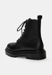 Stivaletto in pelle nera alla caviglia con punta rotonda, lacci anteriori, suola in gomma spessa e texture liscia. Presenta un'etichetta sul retro.