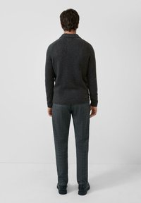 Szary sweter z dzianiny z kołnierzem, zestawiony z teksturowanymi szarymi spodniami w kratę oraz czarnymi butami. Widok od tyłu.