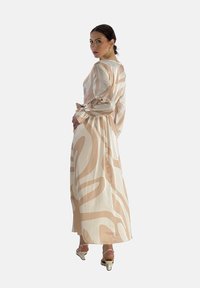 Robe longue et ample en crème avec de grands motifs abstraits beiges. Fabriquée en tissu léger, elle possède des manches longues et une taille cintrée.