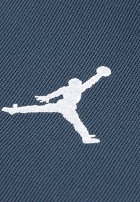 Σκούρο μπλε ύφασμα με υφή που διαθέτει το λογότυπο Jumpman σε λευκό, παρουσιάζοντας μια φιγούρα σε μεσαίο άλμα που κρατάει μια μπάλα μπάσκετ.