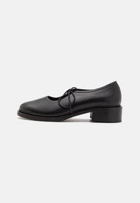 Black leather shoe with rounded toe and a lace-up design. Features a medium block heel and smooth texture. Simple and classic silhouette.
