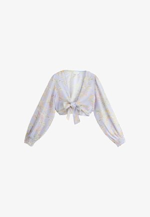 Primer plano de los labios y el hombro de una mujer que lleva una blusa lavanda con un patrón floral tropical detallado en tonos suaves.