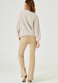 Beige geribbelde trui met een vrije schouderlijn, gecombineerd met lichtbeige flare jeans. Het materiaal lijkt zacht en heeft een iets gestructureerde afwerking.