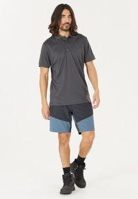 Mörkgrå polo skjorta med korta ärmar och svarta shorts med blå detaljer. Modellen bär svarta stövlar och står mot en vit bakgrund.