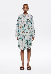 Abito camicia con bottoni in tessuto leggero e trasparente, caratterizzato da una stampa colorata a tema naturale. Maniche lunghe, orlo curvo e vestibilità rilassata.