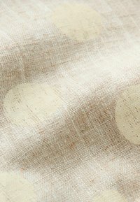 Tissu beige tissé avec de grands motifs circulaires crème subtils, montrant la texture et de légers plis.