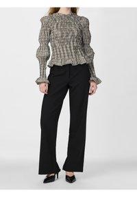 Woman wearing a black and beige checkered smocked blouse with ruffled cuffs and neckline, black high-waisted wide-leg pants, and black heels.