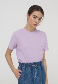 T-shirt in cotone lavanda con maniche corte, scollo rotondo e tasca con design "HUG me". Abbinato a pantaloni shorts in denim blu.