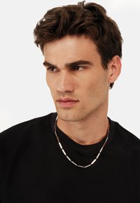 Silvrfarvet metallinkekæde med rektangulære led, der har skiftevis polerede og matte overflader, båret over en sort T-shirt.
