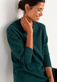 Dunkelgrüner, strukturiert gestrickter Pullover mit lässiger Passform und Dreiviertelärmeln. Das Modell ist dezent gestylt mit minimalem Schmuck.