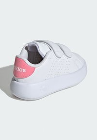 White sneaker with pink heel accent, Velcro straps, perforated sides, smooth leather texture, and a rubber sole.