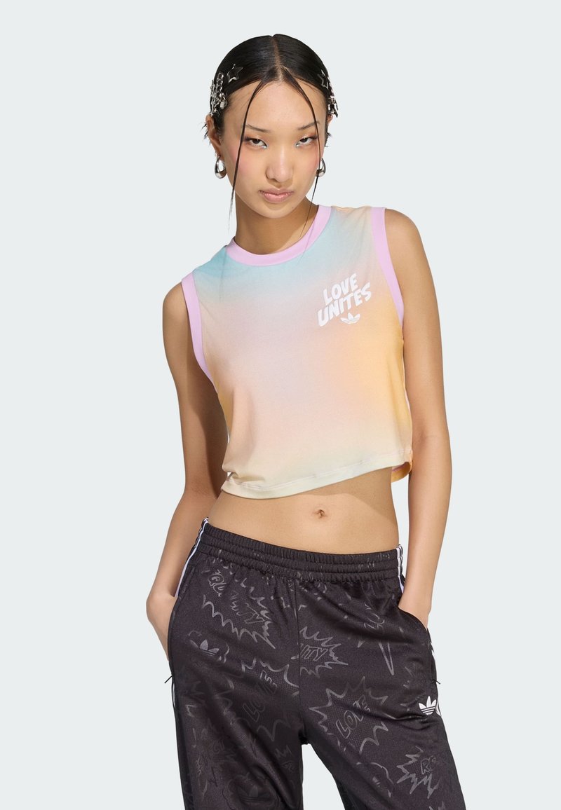 Ung kvinde med stjerne hårklemmer bærer en ærmeløs pastel crop top med teksten "LOVE UNITES" og sorte mønstrede træningsbukser med hænderne i lommerne.
