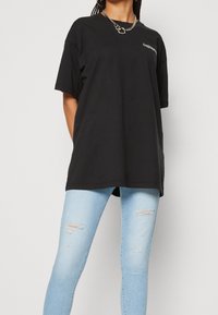 Camiseta negra de gran tamaño con mangas cortas, que presenta un pequeño logo blanco. Combinada con vaqueros ajustados de mezclilla azul claro desgastados.