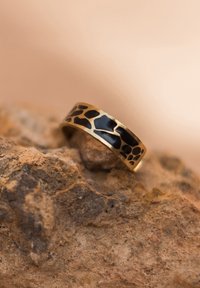 Bague en or avec une incrustation noire à motif au fini semi-mat, sur fond rocheux.