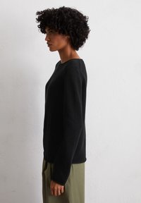 Schwarzer, strukturierter Pullover mit Rundhalsausschnitt, langen Ärmeln und lockerer Passform, kombiniert mit olivgrünen Hosen.