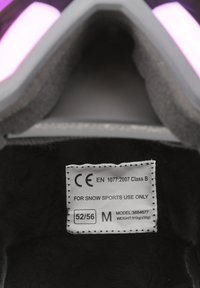 Indvendig på en sort snesports hjelm, der viser et blødt for, med et mærke, der viser CE-certificering, modelnummer, størrelse 52/56 og vægt 510 g.