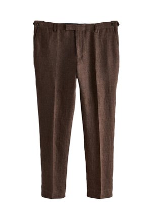 Braune Leinenhose mit einer geknöpften Gesäßtasche, kombiniert mit einem grünen Leinenhemd, das hineingesteckt ist.