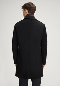 Zwarte jas met een gladde afwerking, met een getailleerde snit, een middellange uitvoering en een klassieke kraag. Getextureerde stof met zijzakken.