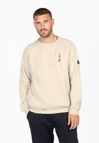 Felpa beige con maniche lunghe, collo a girocollo e tasca sul petto con zip. Presenta polsini e orlo a coste, realizzata in morbido tessuto testurizzato.