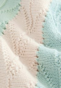 Strickdecke mit einem strukturierten Muster in Pastellrosa und Hellblau, mit gewellten Rändern und weichem, gemütlichem Garn.