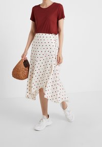 Maglietta rossa a maniche corte abbinata a una gonna avvolgente bianca con pois rossi, accessorized con una borsa intrecciata e sneakers bianche.