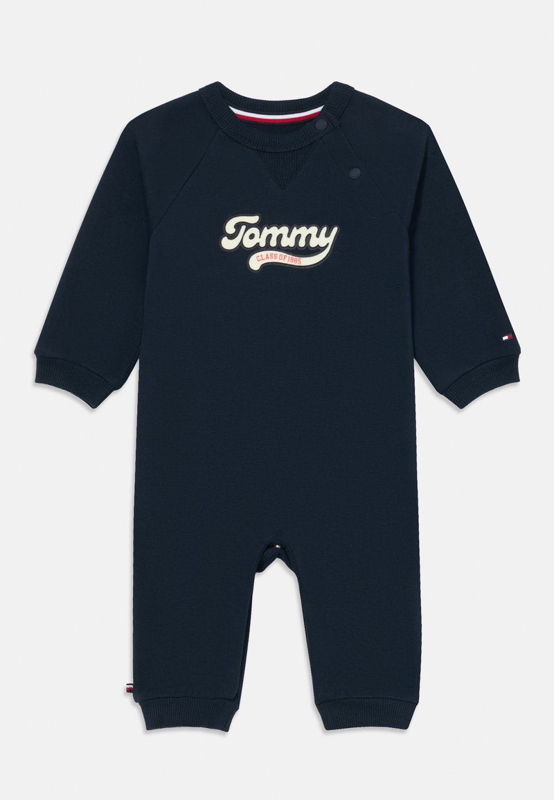 Jūras zila kokvilnas zīdaiņu romperis ar garām piedurknēm, ar spiedpogām uz pleca un izšūtu "Tommy Class of 1985" uz priekšpuses.