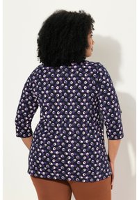 Marineblaues Tunika mit Dreiviertelärmeln, versehen mit einem gemusterten Design aus pinken und lila Kreisen, aus weichem Stoff und in lockerer Passform.
