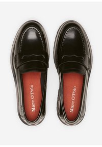 Un par de mocasines de cuero negro con plantillas rojas de la marca Marc O'Polo, vistos desde arriba sobre un fondo blanco.